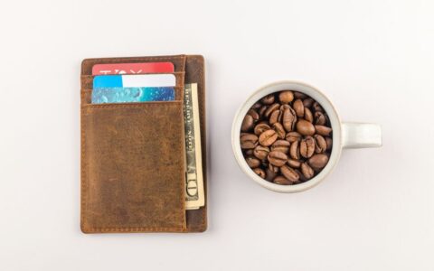 Top view of a leather wallet with credit cards and a cup filled with coffee beans on a white background.