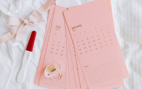 Flat lay of pregnancy test, calendar cards, and baby items symbolizing new beginnings.
