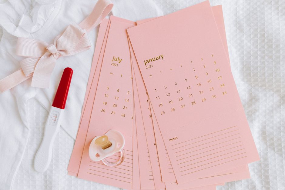 Flat lay of pregnancy test, calendar cards, and baby items symbolizing new beginnings.