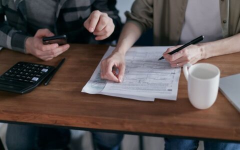 Couple managing finances at home with a calculator, smartphone, and documents.