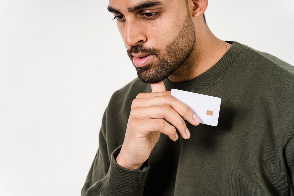 Pensive man in green sweater holds a white credit card against a white background.
