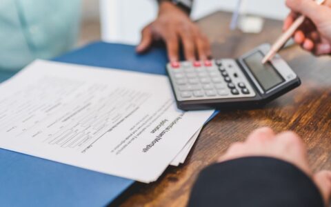 Hands using a calculator with real estate documents on a desk, indicating a financial transaction or meeting.