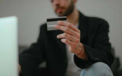 Blurred image of a man holding a credit card, emphasizing online shopping.
