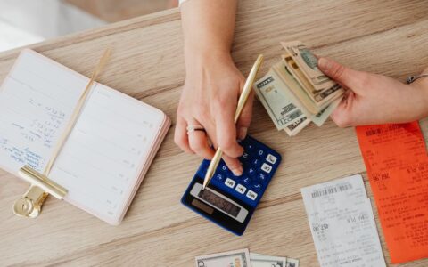 Hands managing finances with calculator, cash, and receipts on a wooden table. Ideal for budgeting concepts.