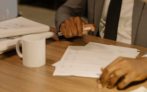 Close-up of a businessman holding and reviewing documents on a wooden desk.