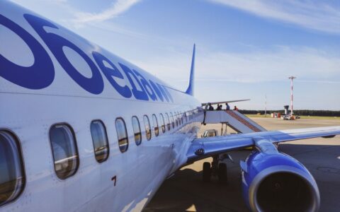 Side view of a commercial airplane with passengers boarding at a sunny airport.