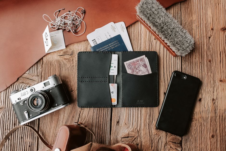 Flat lay of traveler essentials including wallet, camera, and phone on wooden surface.